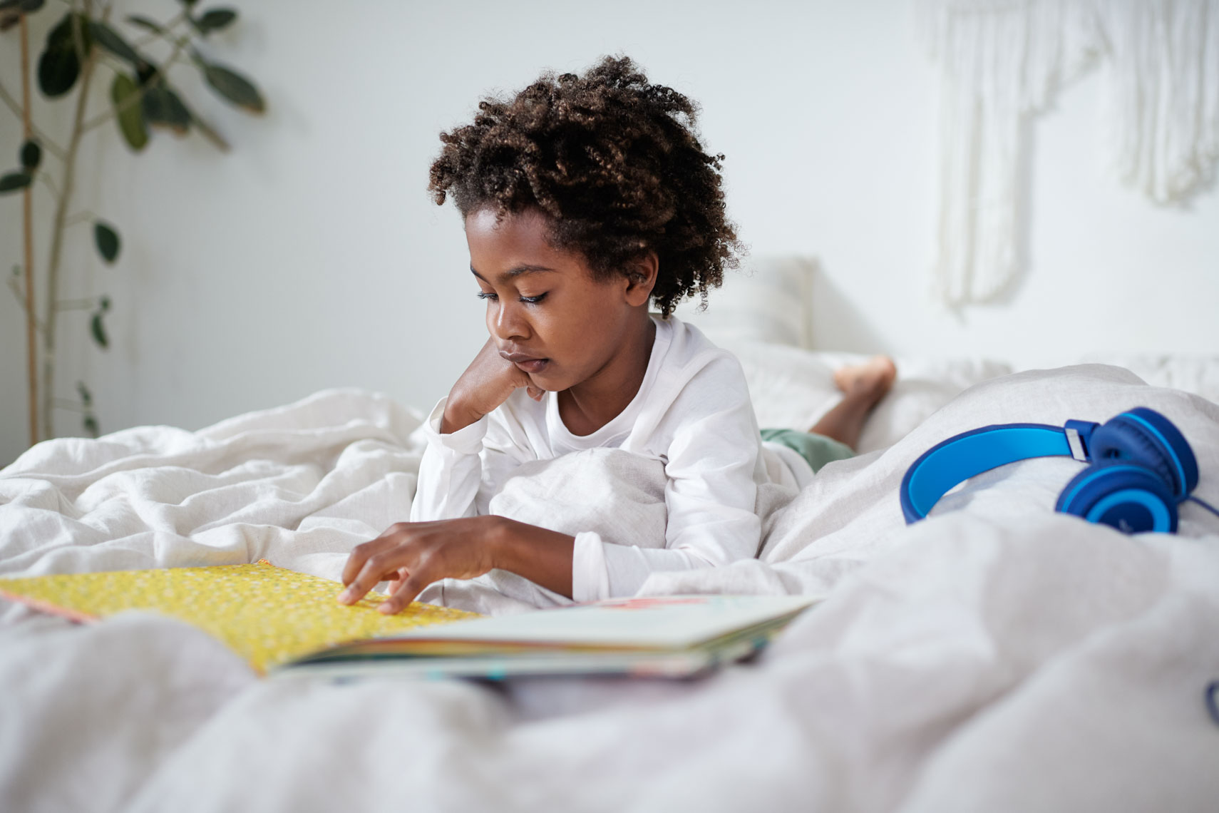 Child reading on bed with headphones 